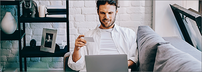 Guy on couch with credit card searching on laptop